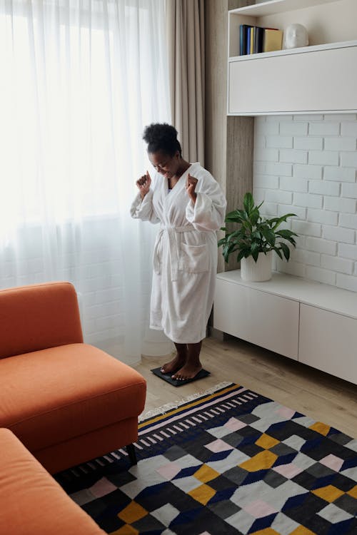 Woman in a Bathrobe Smiling while Standing on a Weighing Scale