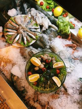 A vibrant display of fresh seafood on ice with fish, shellfish, lemons, and greens in a market setting.