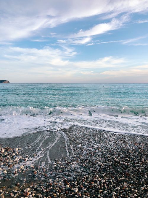 Free Serene view of gentle waves on a pebbly beach in Bečići, Montenegro under a blue sky. Stock Photo