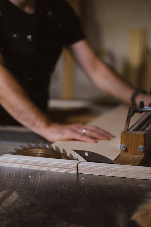 Unrecognizable blurred male master cutting wooden plank using table saw with sharp knives while working in professional workshop with special instruments