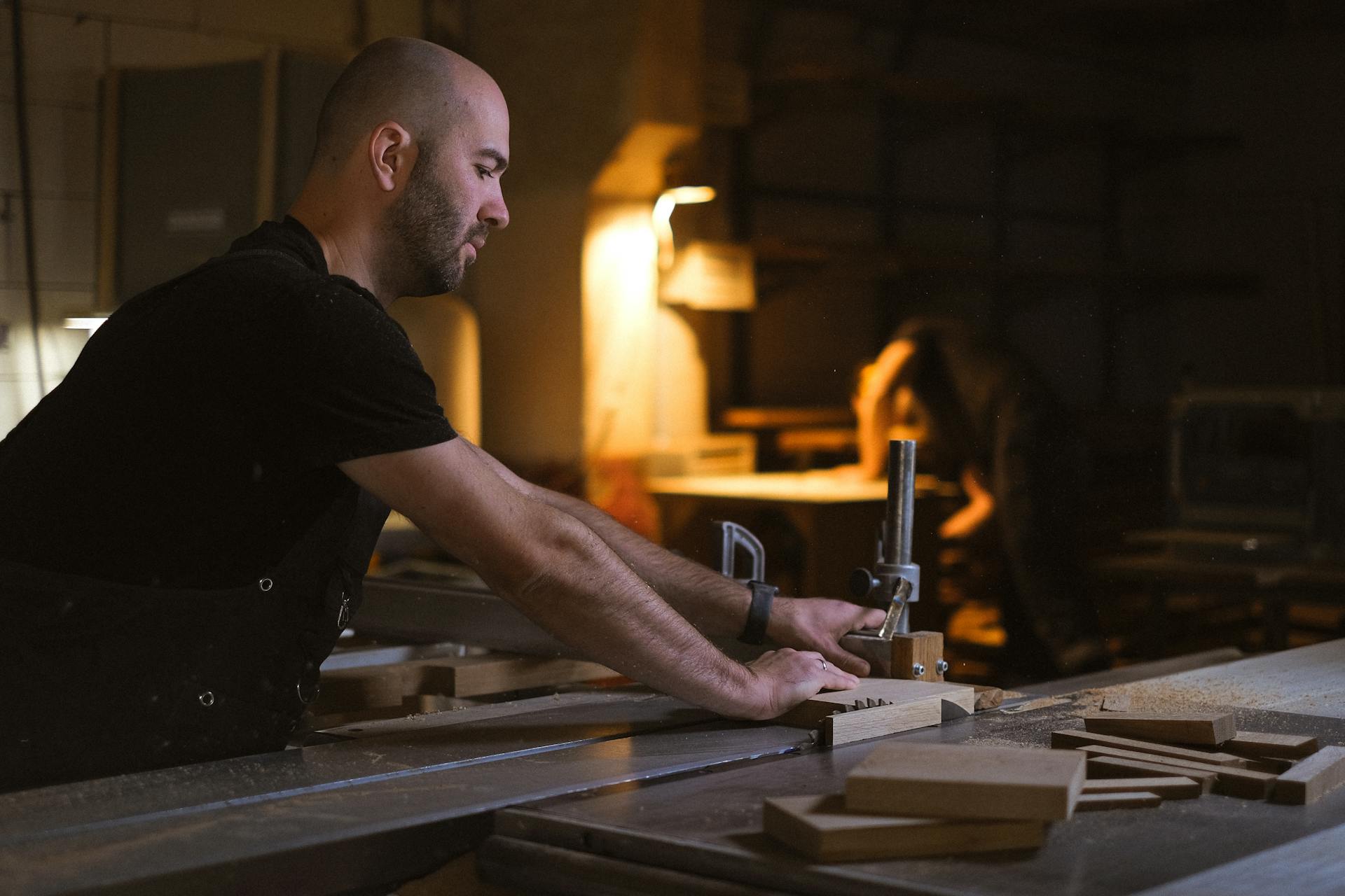 A focused craftsman skillfully operates a saw in a dimly lit woodshop, highlighting artisanal woodworking skills.
