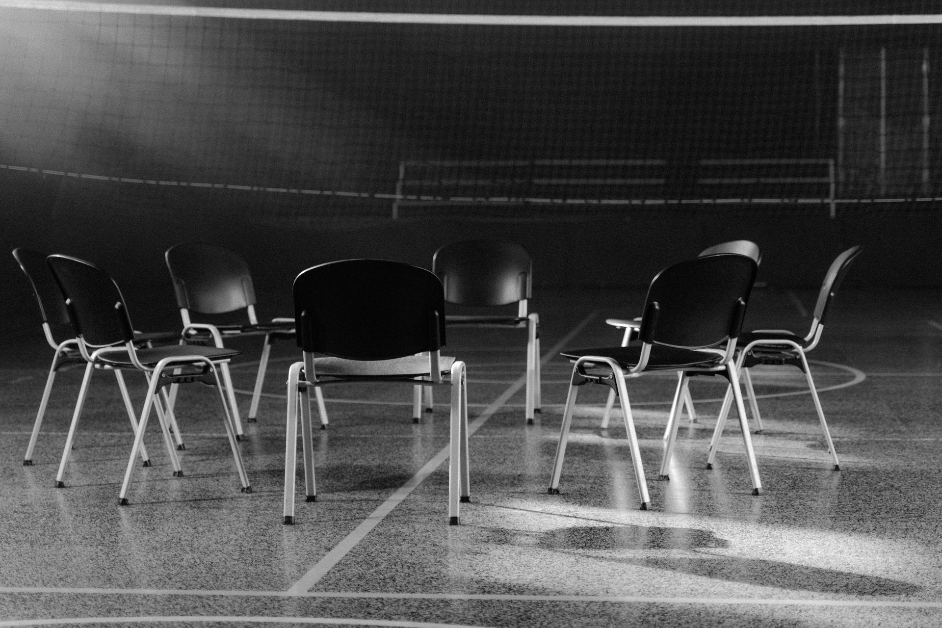 Black and white chairs arranged in a circle on an indoor volleyball court.