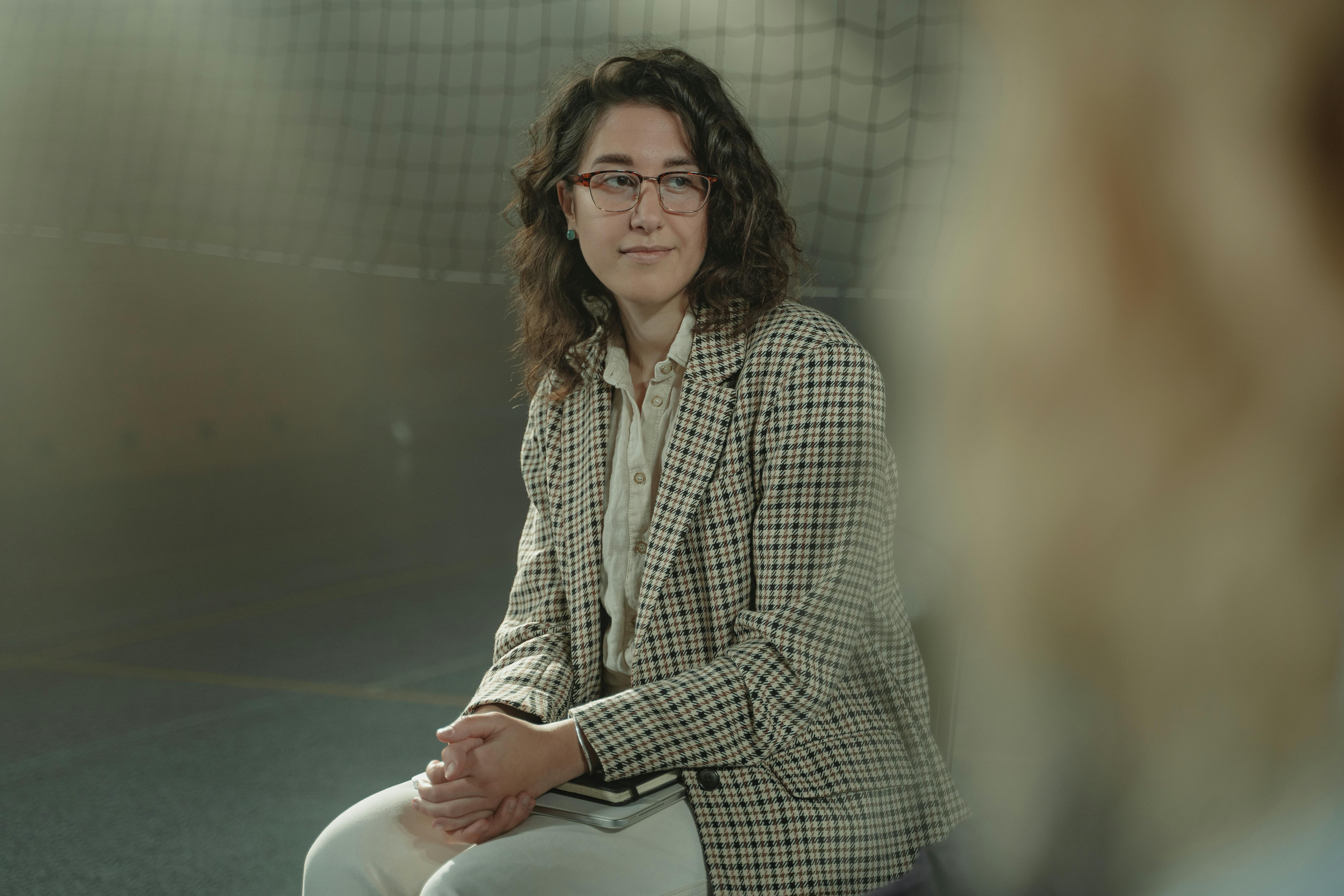 一位戴着眼镜、穿着格子夹克的白人妇女坐在室内，表情沉思