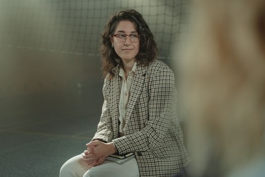 一位戴着眼镜、穿着格子夹克的白人妇女坐在室内，表情沉思