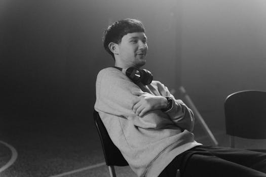 Black and white photo of a young man relaxing indoors with headphones around his neck.