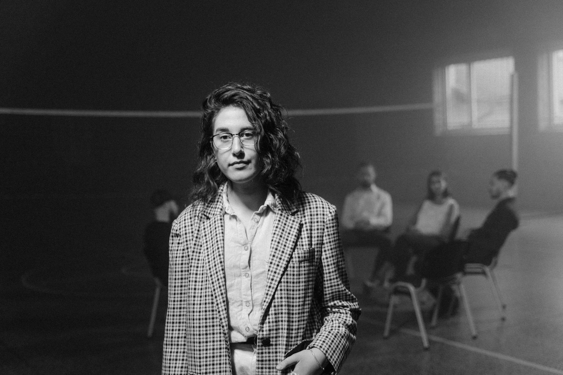 Monochrome image of a woman standing with a support group meeting in the background.