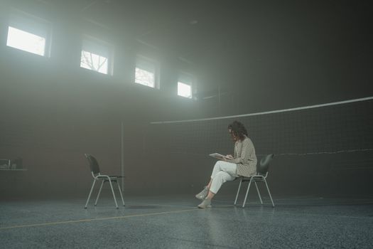 一名女子在健身房里，坐在一张带有椅子和网的平板电脑前