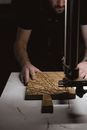 Unrecognizable male master standing at workbench with metal industrial bandsaw machine while working with wooden plank in professional joinery in darkness