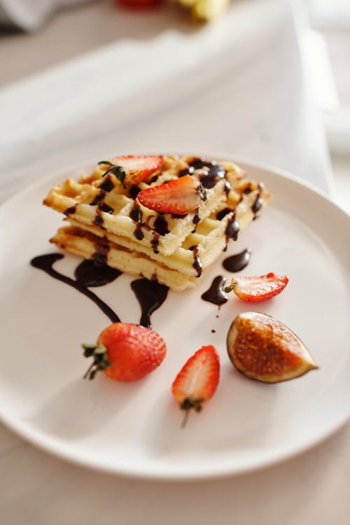 Free Tasty waffles drizzled with chocolate syrup, topped with fresh strawberries and figs on a white plate. Stock Photo