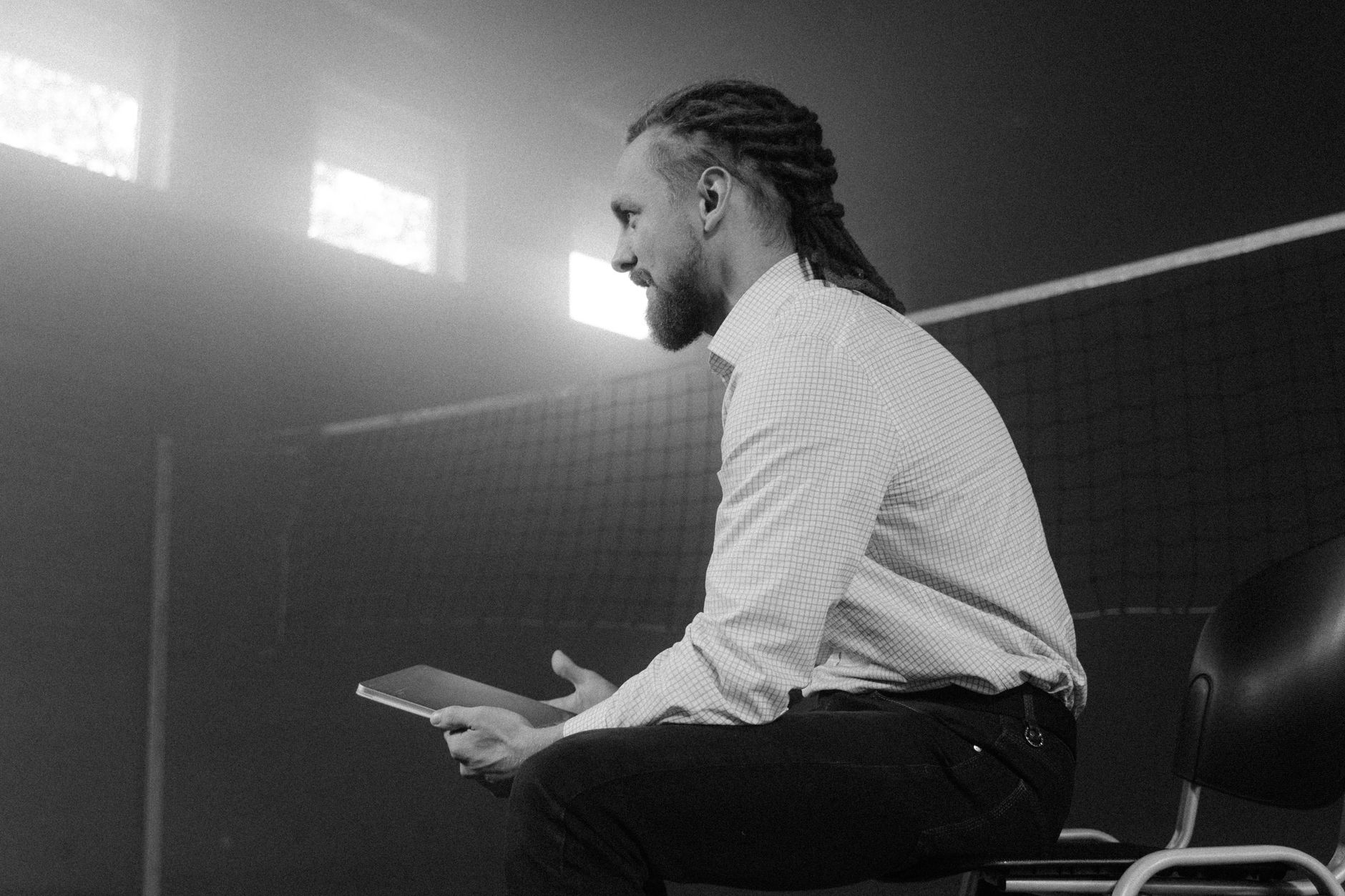 A man with dreadlocks sits in a smoky, well-lit room holding a device.