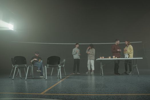 A group of people having a casual discussion in a smoky indoor setting with chairs and a table.