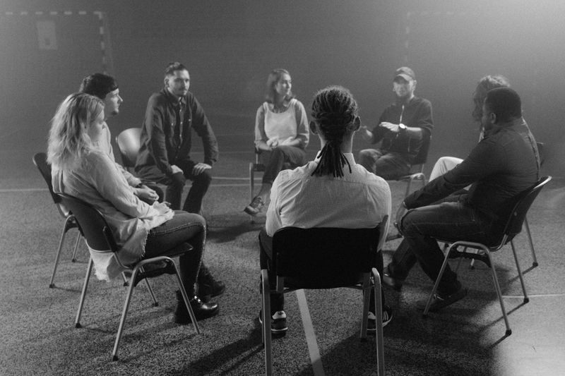 A diverse group of people in a circle discussing and supporting each other in a therapy session