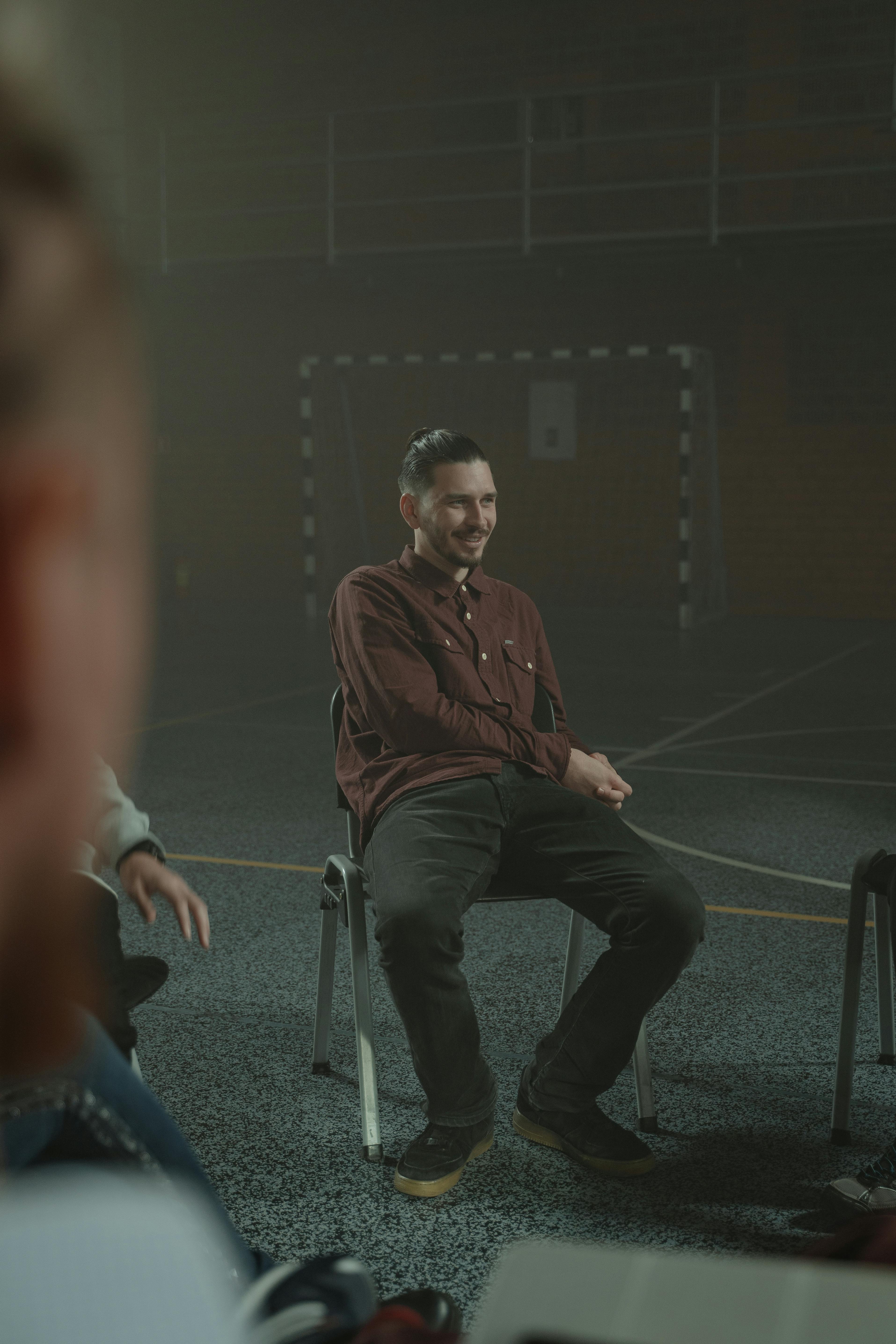 Adults engaged in a group therapy session inside a dimly lit, smoky room.