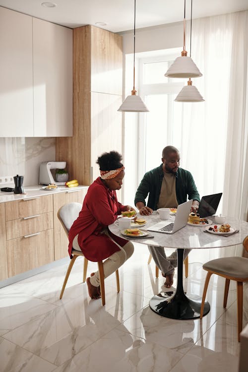 Free Couple In the Kitchen Table Using their Laptops Stock Photo