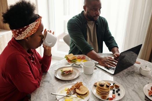 Man typing on laptop and woman drinking coffee during breakfast.