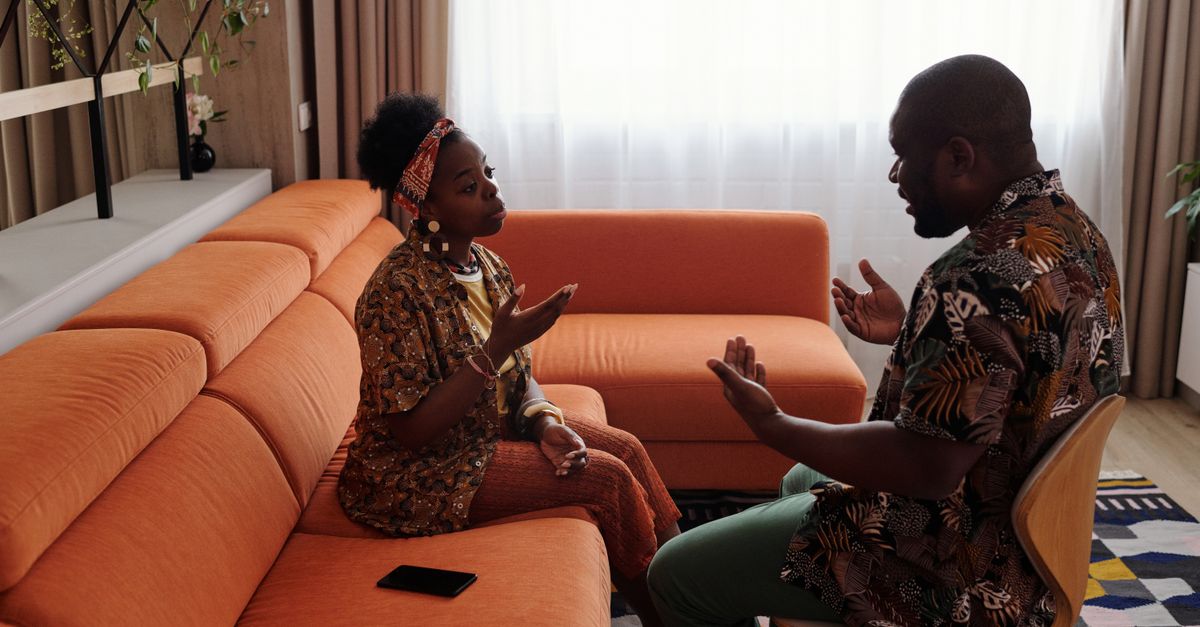 A couple having an emotional discussion on an orange sofa in modern living room.