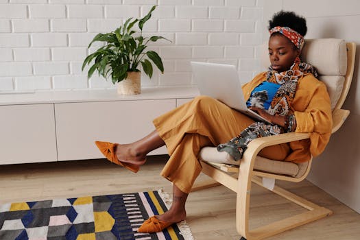 An African American woman in colorful attire works on her laptop from a cozy home office setup.