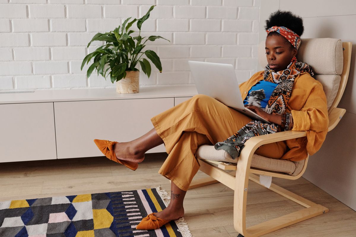 A woman works on her laptop from an armchair in a bright home office
