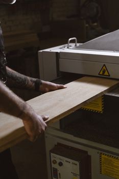 Crop anonymous male working with timber plank and using metal lathe in workshop
