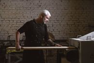 Focused mature man loading wooden plank in metal turning machine