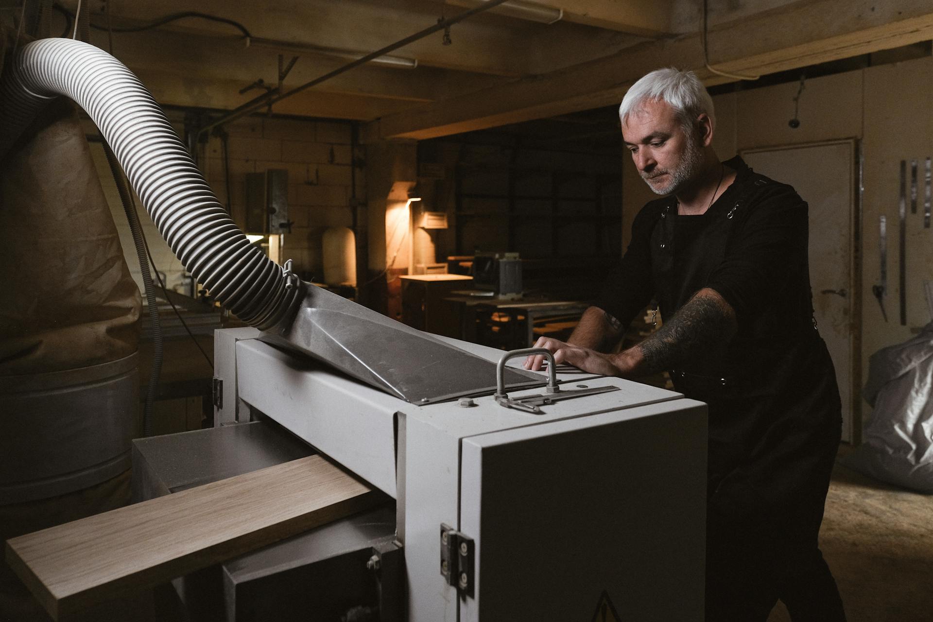 Thoughtful middle aged skillful male working with metal turning machine in spacious workshop