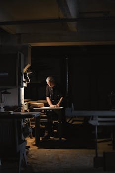 Artisan focusing on woodworking in a dimly lit workshop, highlighting craftsmanship.