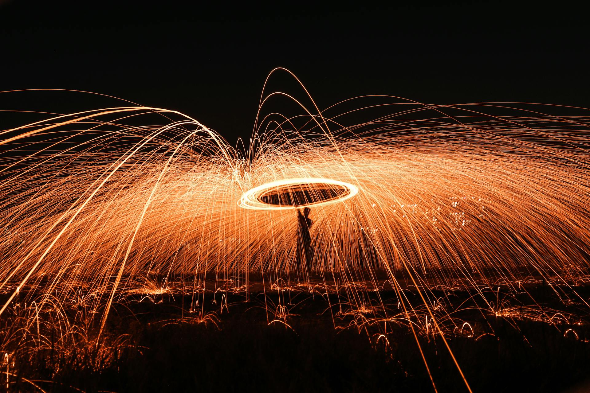 Captivating long exposure of steel wool spinning at night, creating dynamic light trails and sparks.