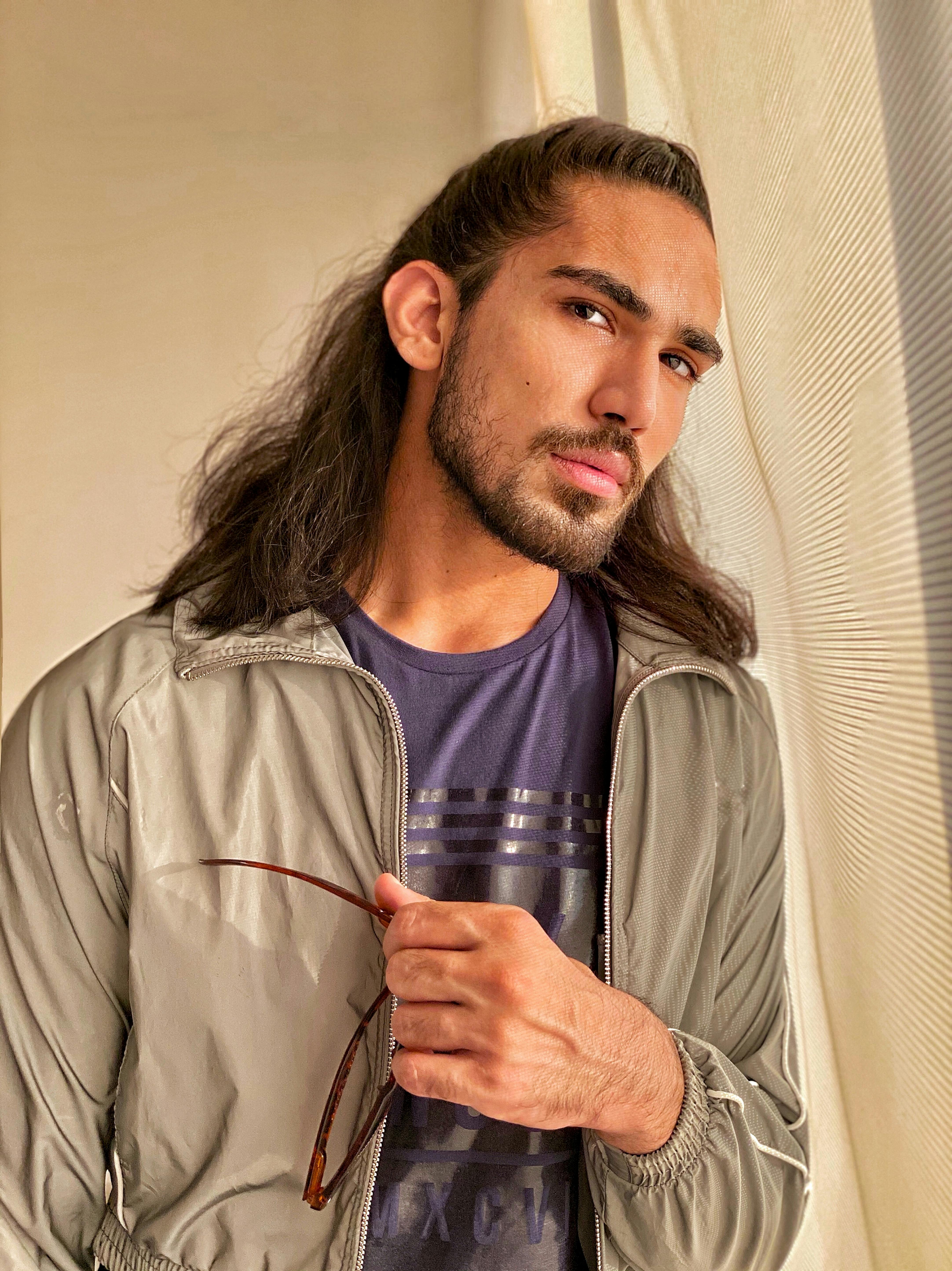 Trendsetting young man with long hair and sunglasses enjoying natural light indoors.