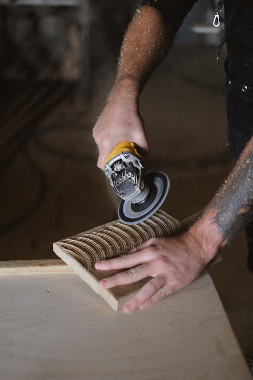 Crop craftsman creating patterns on wooden board with angle grinder