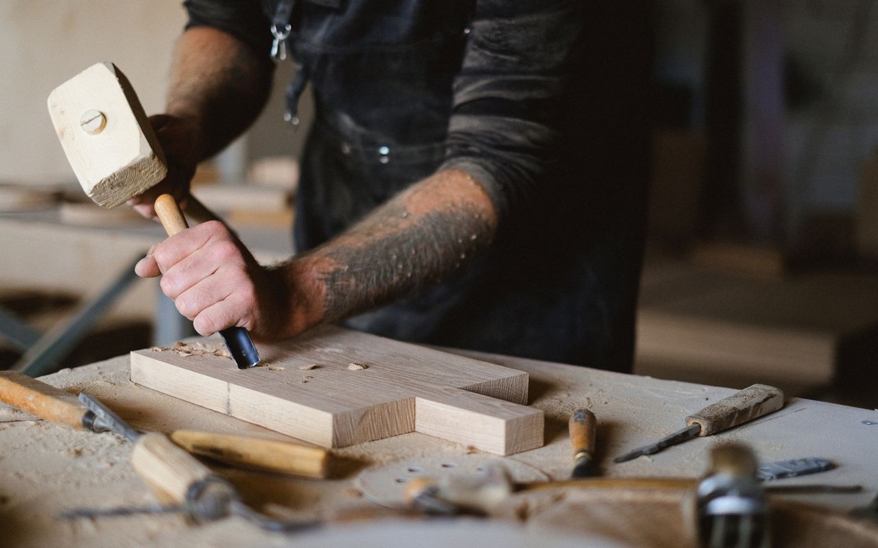Joiner with mallet and chisel on pale timber, workshop