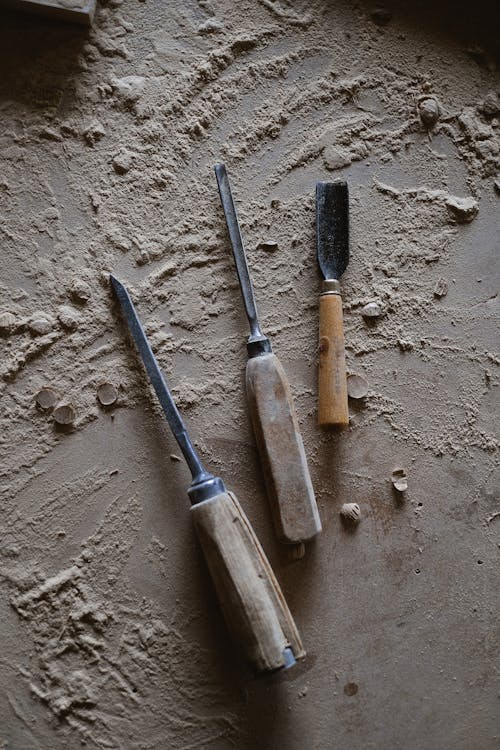 Top view of different special tools for carving wood with wooden handles placed on messy table with shavings in professional joinery