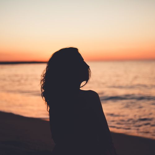 Free Silhouette of faceless female standing on beach of ocean at bright colorful sundown Stock Photo