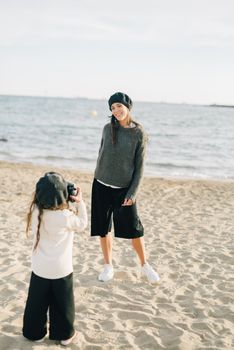 A mother poses for her daughter taking a photo at the beach under bright daylight.