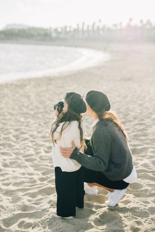 Free A mother and daughter enjoy a sunny day at the beach, capturing moments with a camera. Stock Photo