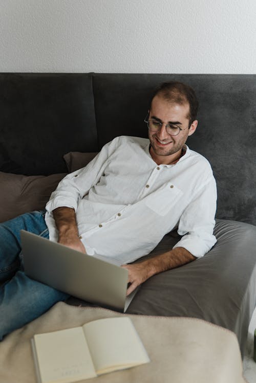 Man in White Dress Shirt Using Laptop in Bed