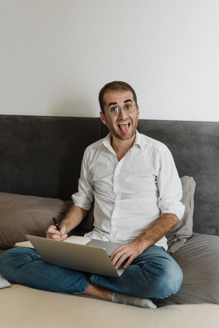 Man working joyfully from home with a laptop, showing playful expression. Man working joyfully from home with a laptop, showing playful expression.