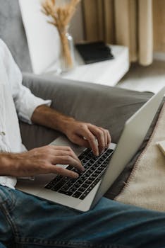 Close-up of a person typing on a laptop indoors in a cozy home environment.