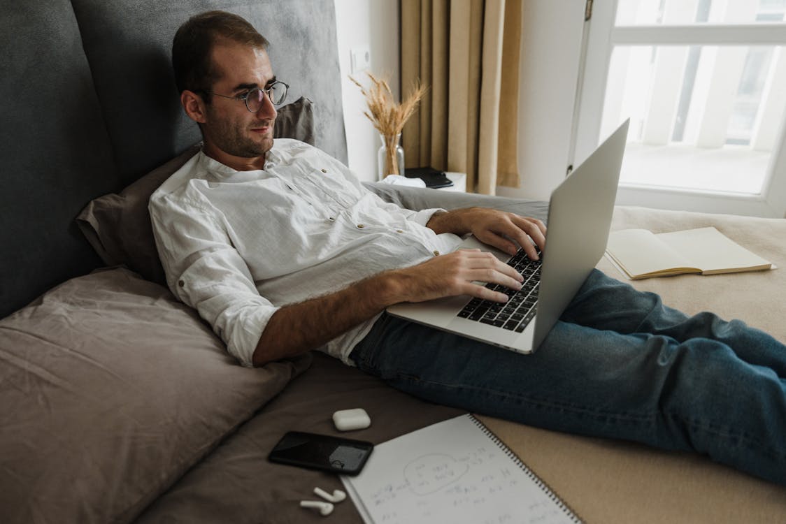 Homem De Camisa Branca Com Botões Usando Macbook Air No Sofá Marrom