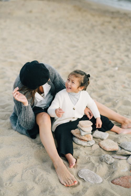 Free Mother and Daughter Sitting on Sand at the Beach Stock Photo