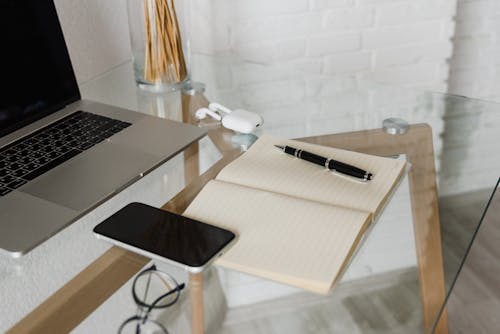 A Cellphone on Notebook with a Pen Beside an Airpods