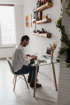 Man concentrating on work at home office desk with laptop and decor. Cozy setting with natural light.