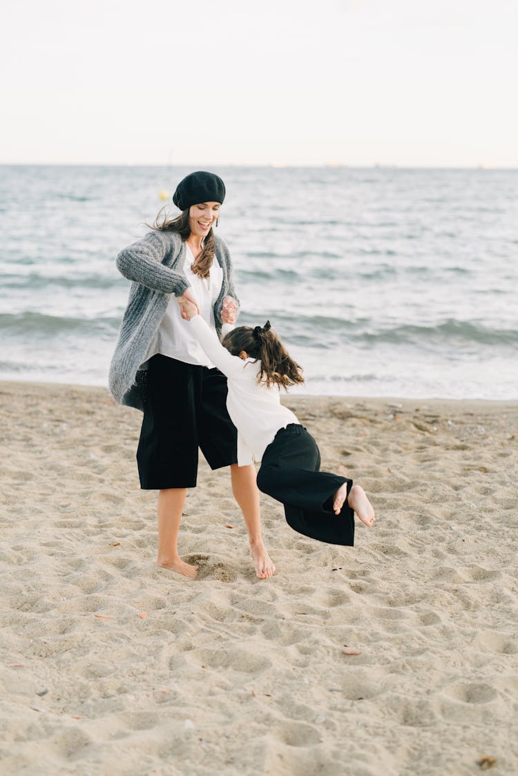 A Woman Swinging A Kid By The Hands On The Shore
