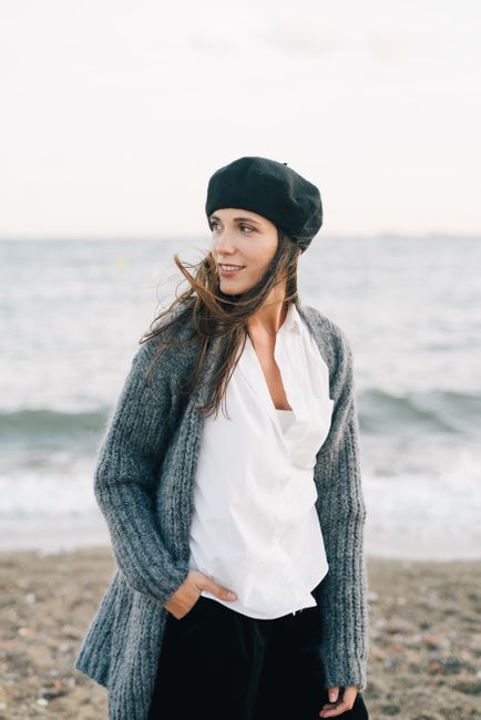 Young woman in a gray sweater and beret enjoying a breezy beach day.