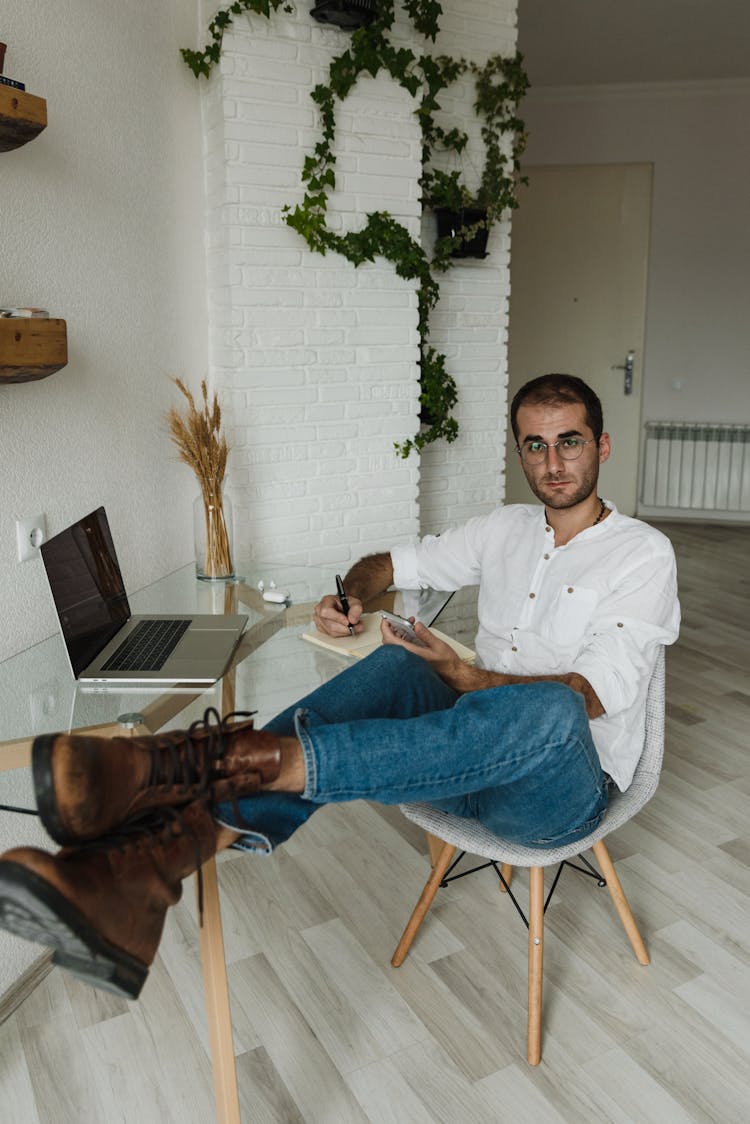 A Man In White Dress Shirt Sitting With Feet On Glass Desk