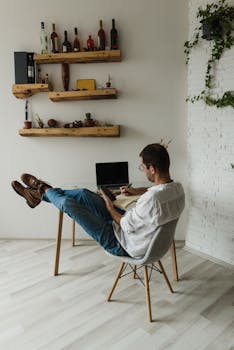 Man working on laptop in a relaxed home setting with stylish shelf decor.