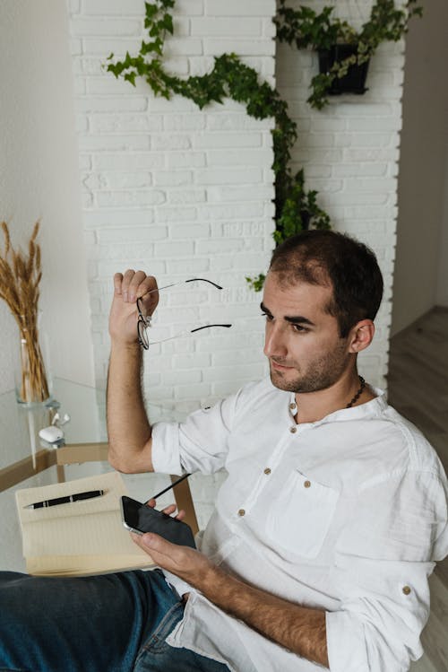 A Man Sitting on a Chair Holding a Cellphone and Eyeglasses while Looking Afar