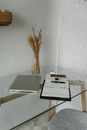 From above of modern netbook placed on transparent glass table near opened planner and smartphone with vase with dried branches