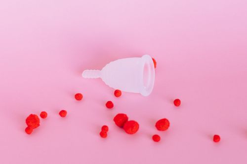 Free Silicone menstrual cup with red decorative elements on a pink background, symbolizing feminine hygiene and eco-friendliness. Stock Photo