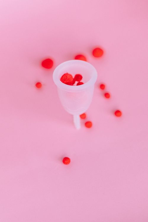 Free Artistic shot of a menstrual cup with red pom poms highlighting feminine hygiene concept. Stock Photo