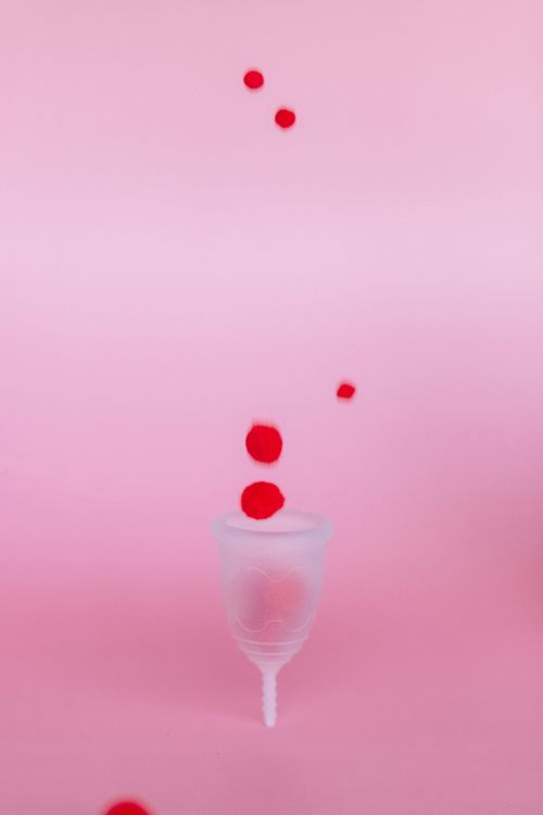 Free A menstrual cup set against a pink background with red dots, symbolizing menstruation. Stock Photo